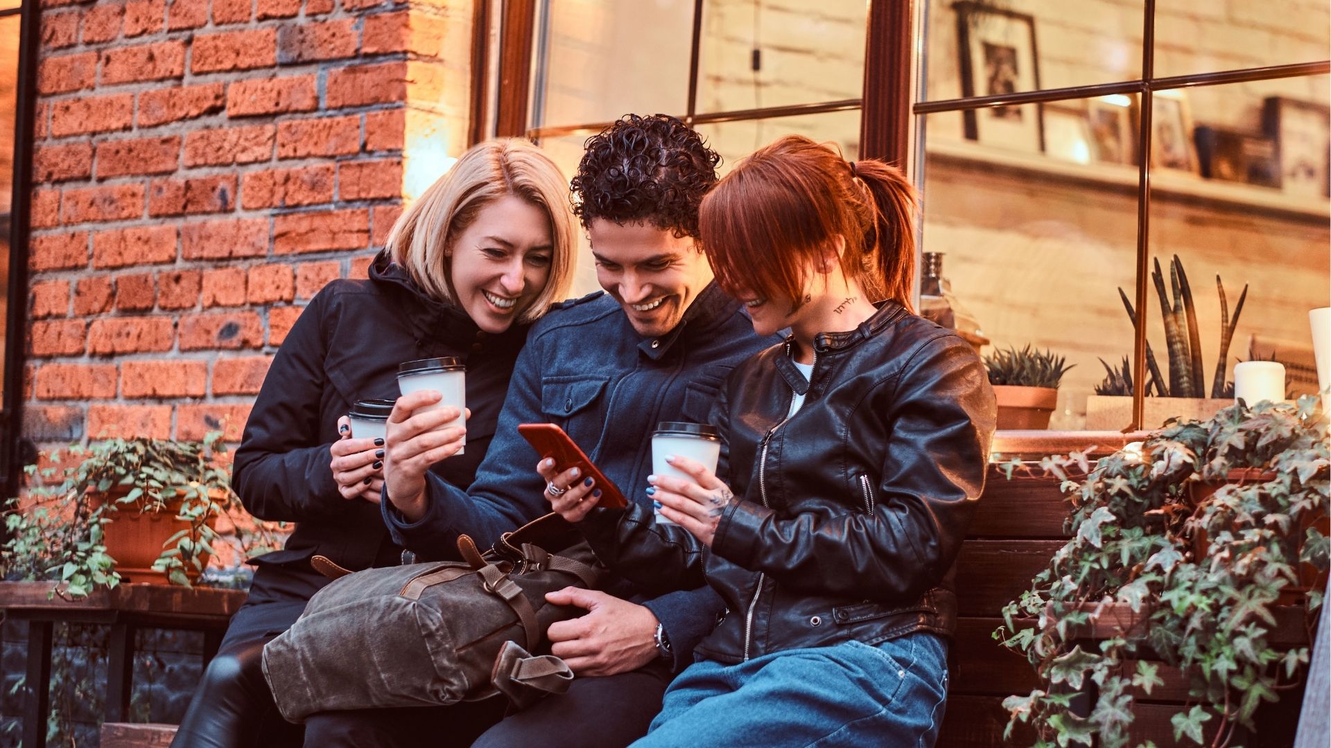 Three happy friends having a break with coffee sitting near a cafe outside