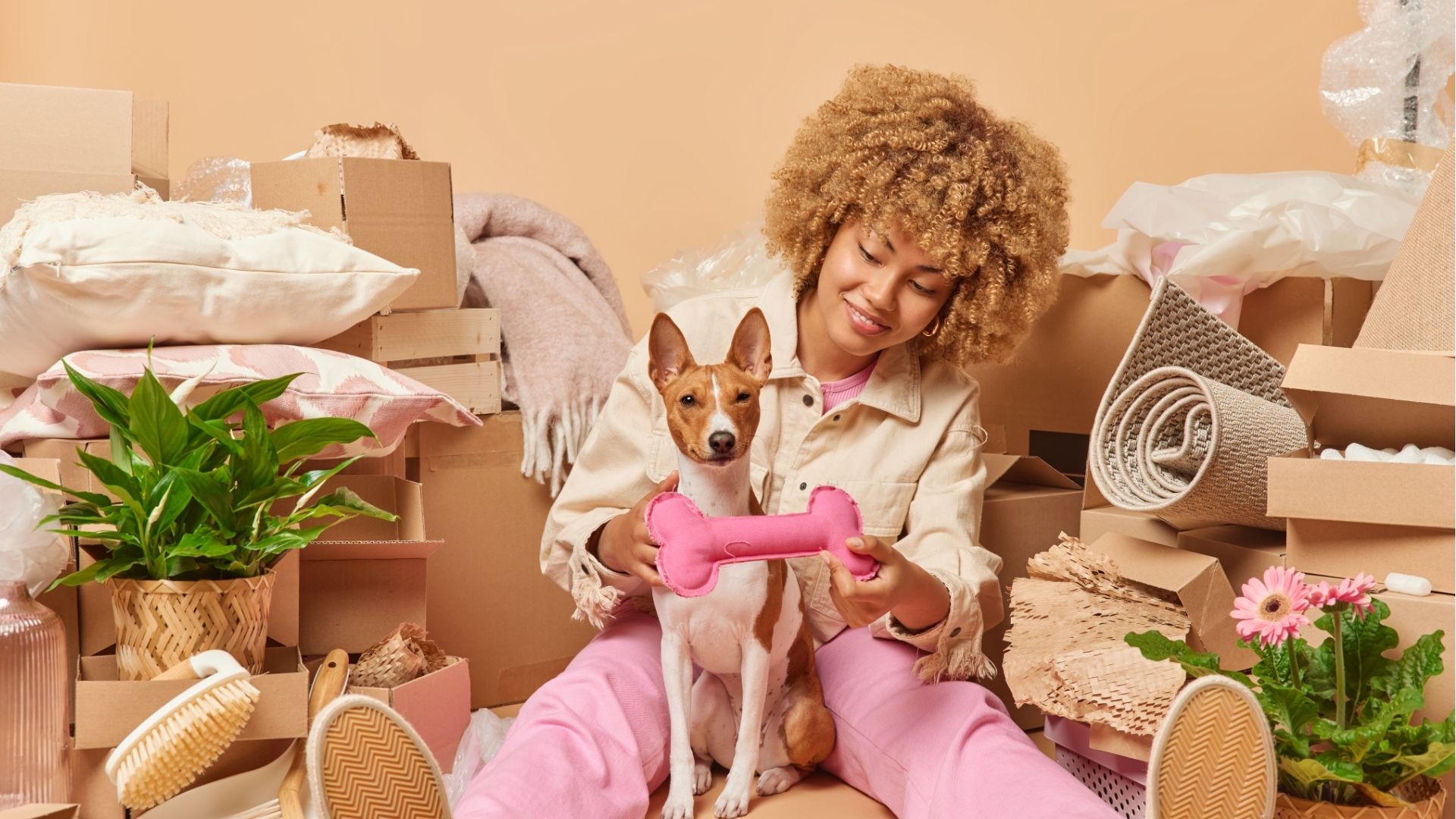 Woman playing with dog with bone toy near cardboard boxes indoors