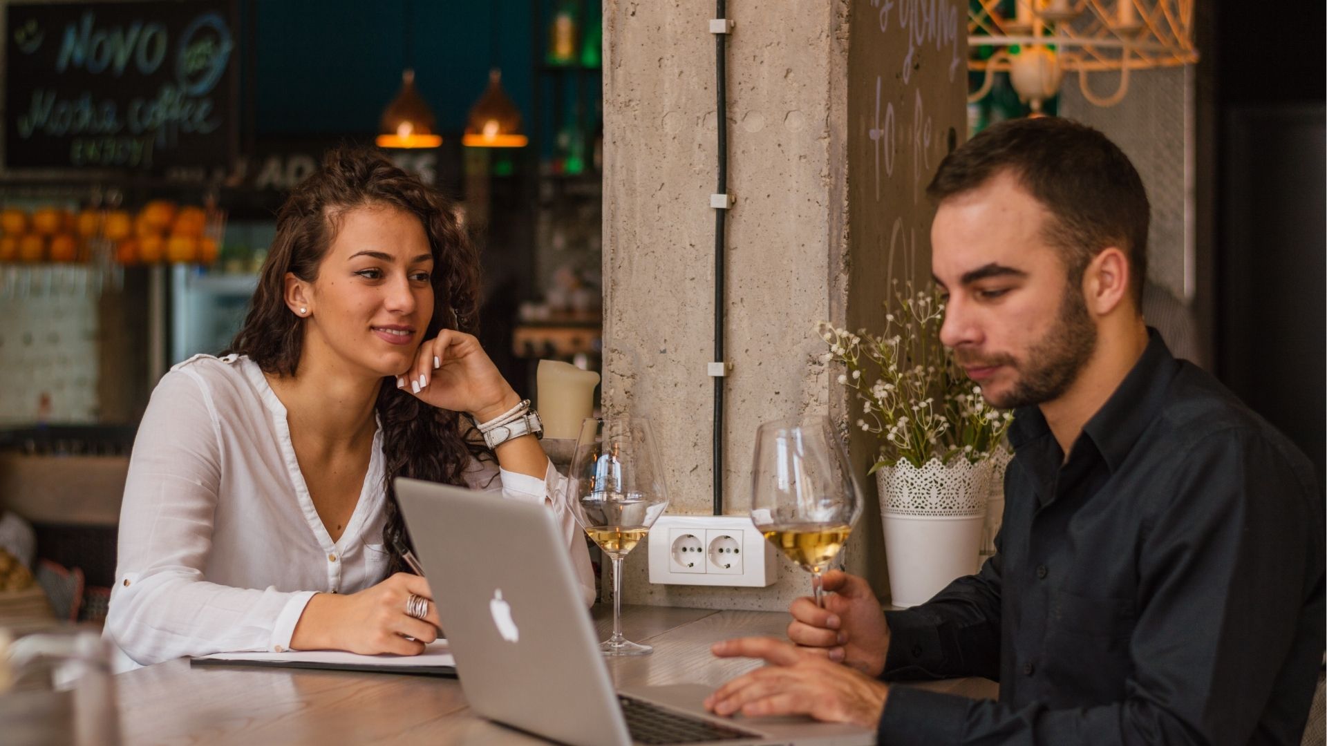 Two business colleagues having a meeting at the restaurant, drinking wine, using a laptop.