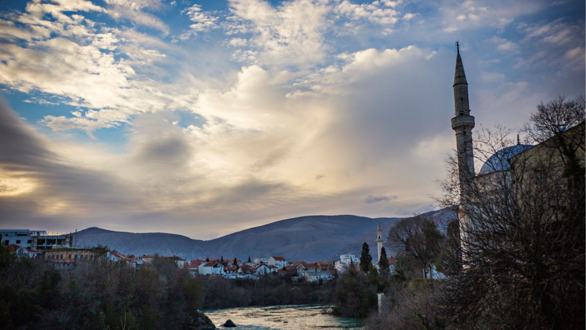 View Of Mostar Town At Sunset, Minarets And Old Houses Against Evening Sky