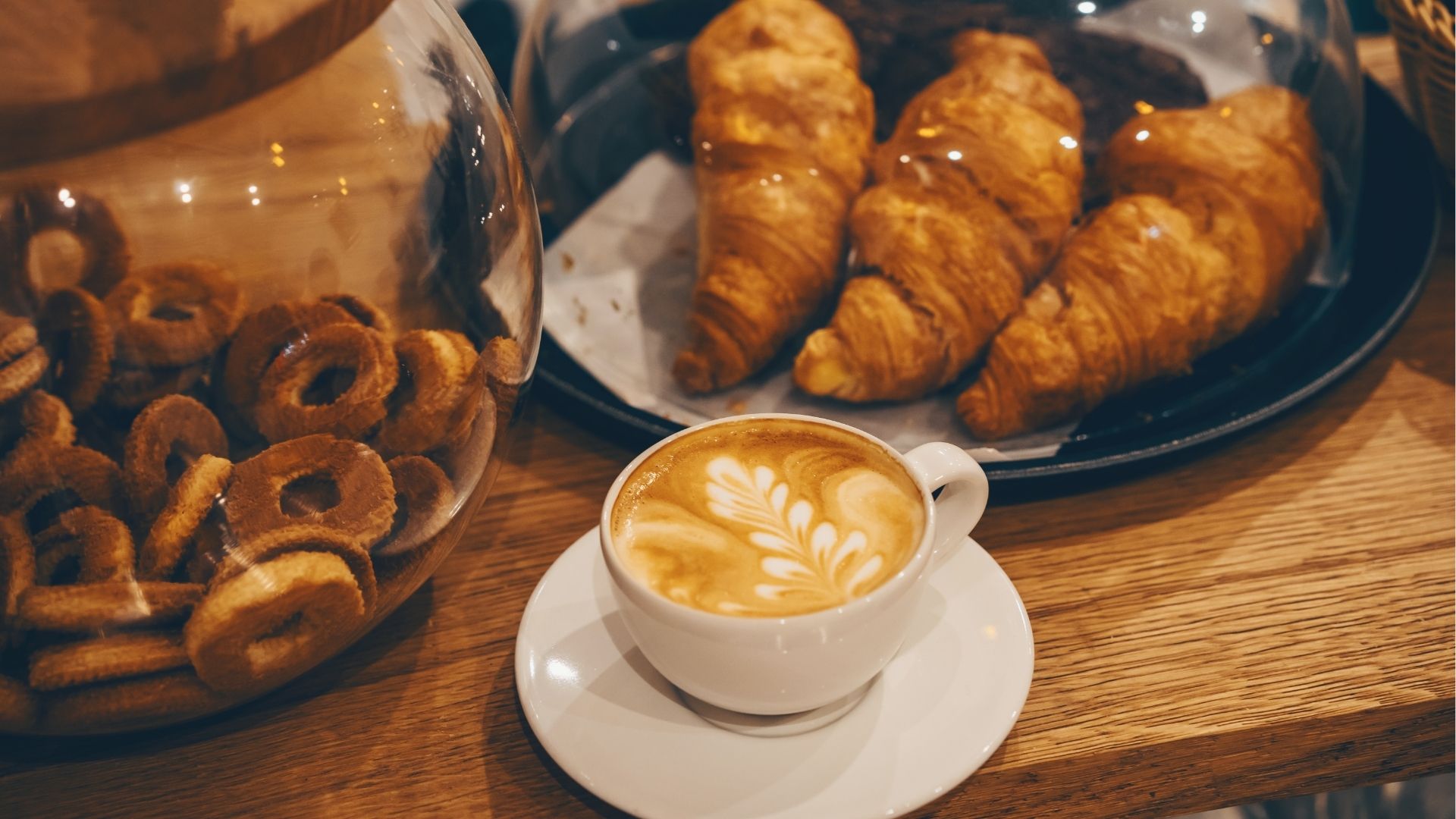 Coffee cup latte art, croissants and biscuit at the bar counter at the bakery and coffee shop