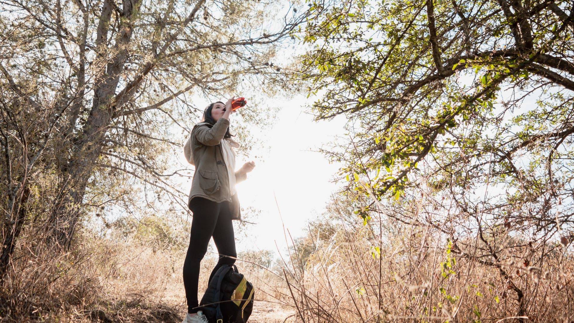 Female solo traveler standing on a hillside and drinking water from her bottle