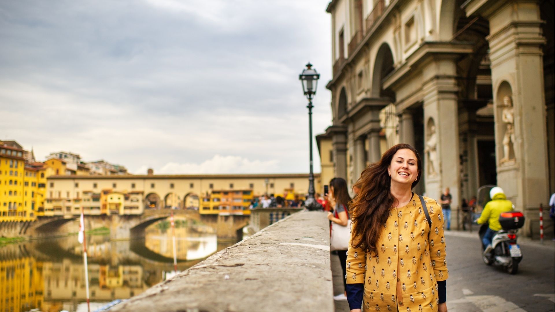 A tourist girl with an orange coat happily walks on the embankment in Florence, Italy