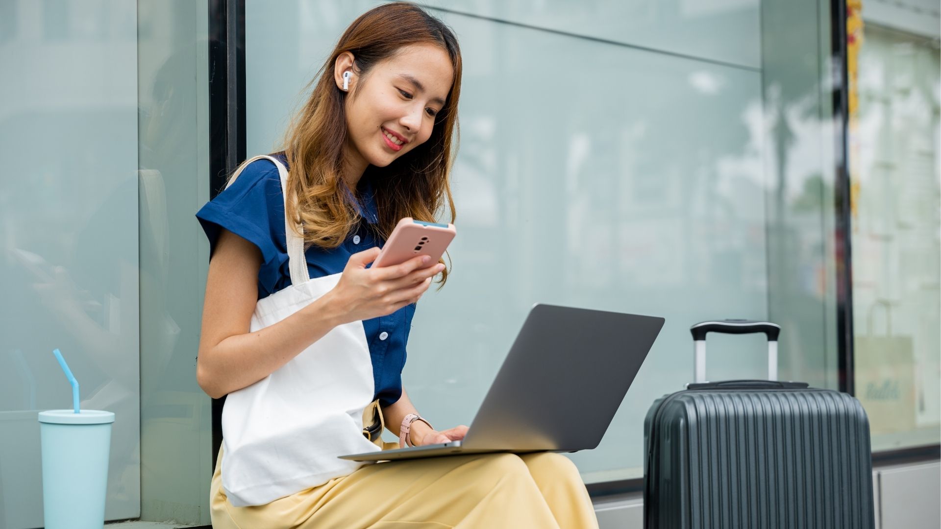 A girl works remotely from a train station, with her laptop and luggage beside her