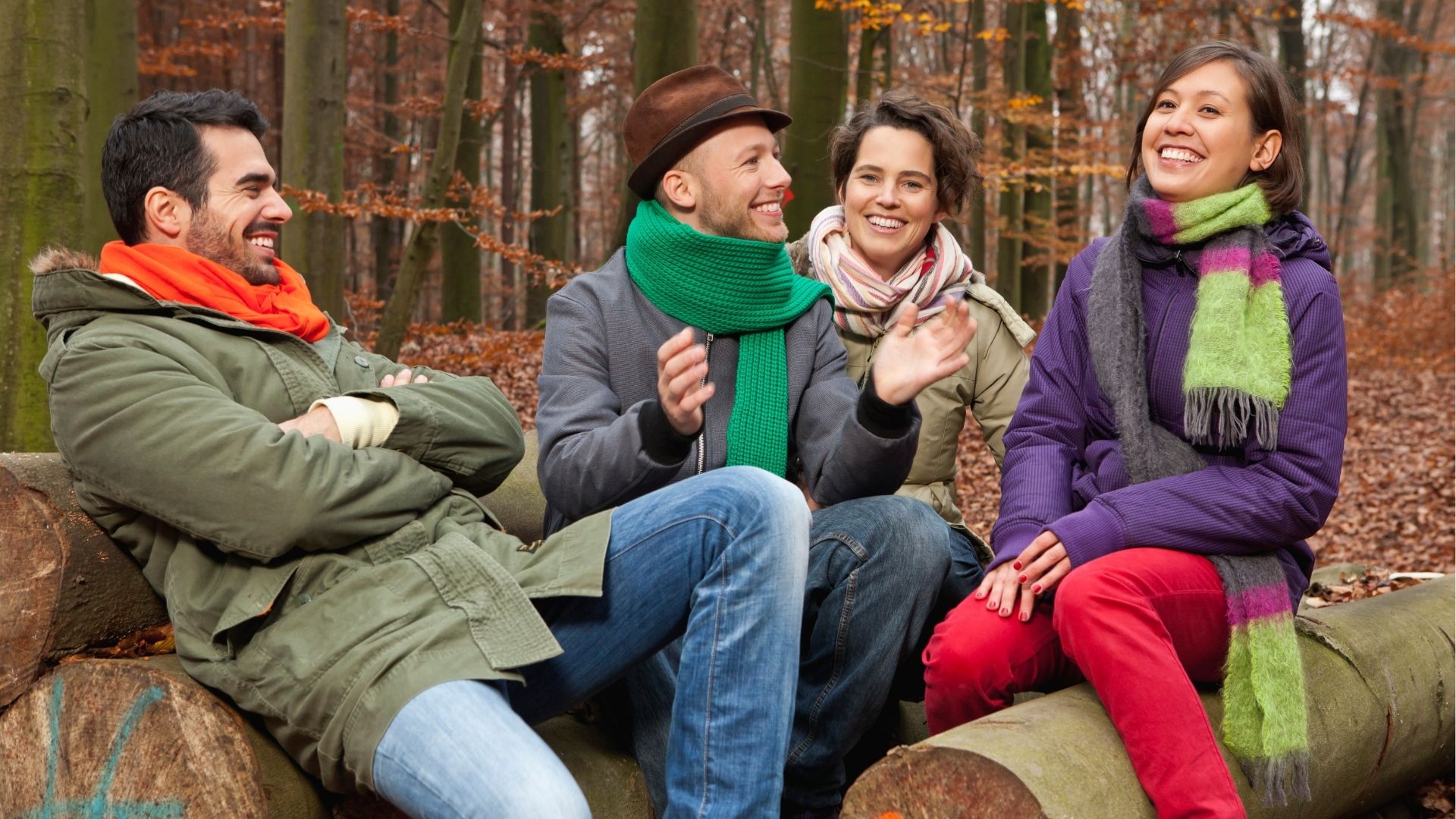 Germany, Berlin, Wandlitz, Men and women sitting on tree trunk, smiling