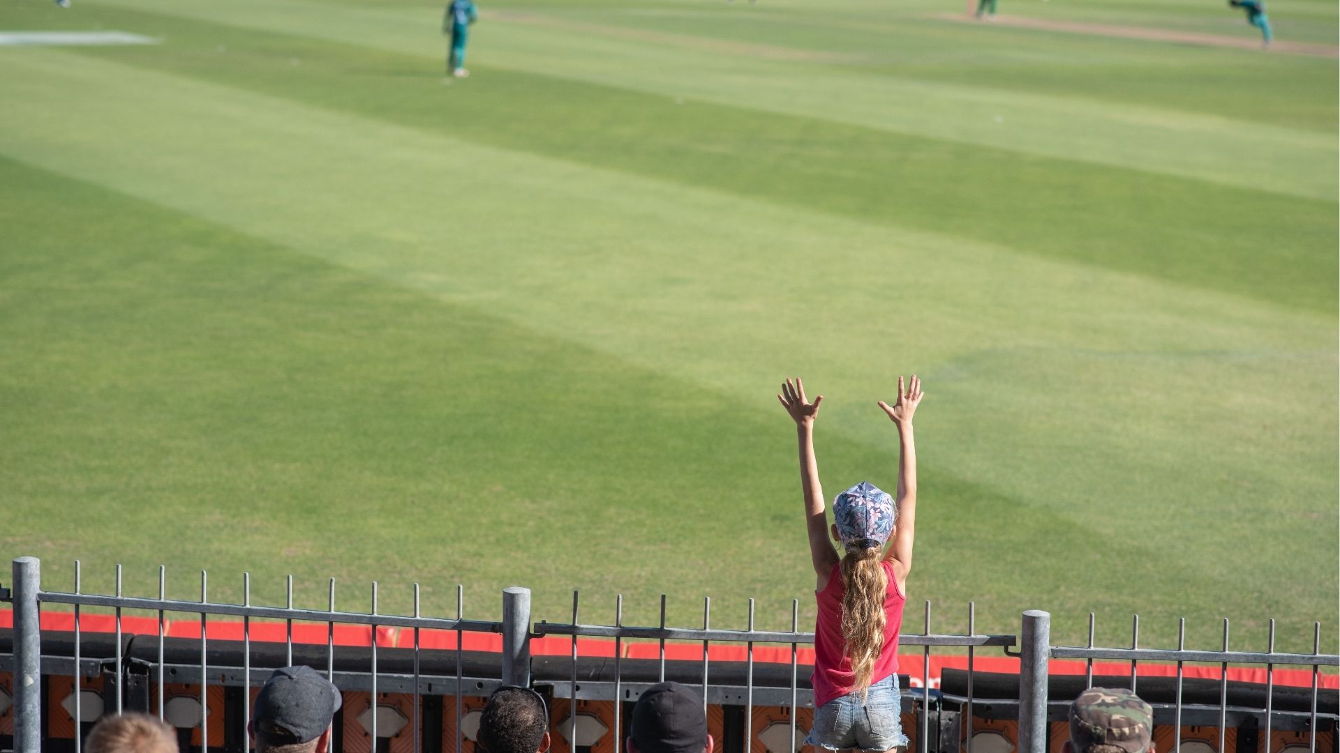 Young fan throwing up her hands in excitement at cricket game
