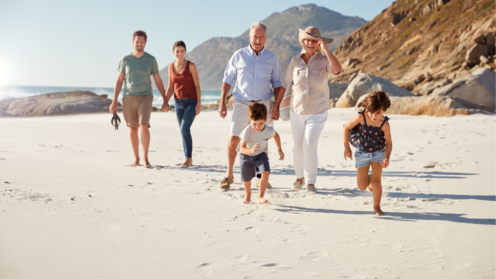 Three generation family walking together on a sunny beach, kids running ahead
