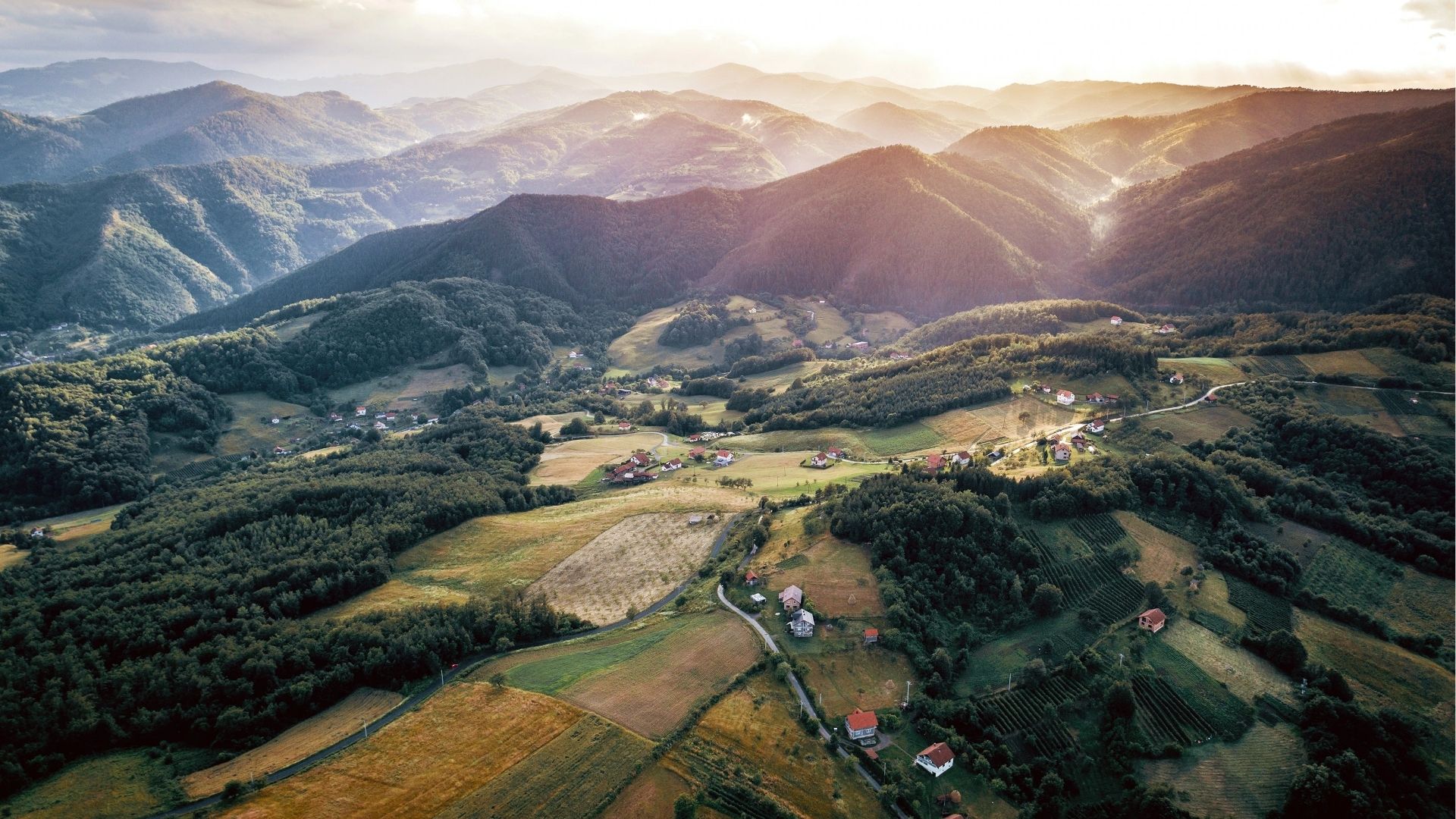 Aerial view of Zenica’s surrounding mountains, valleys, and scattered rural homes under soft sunset light.