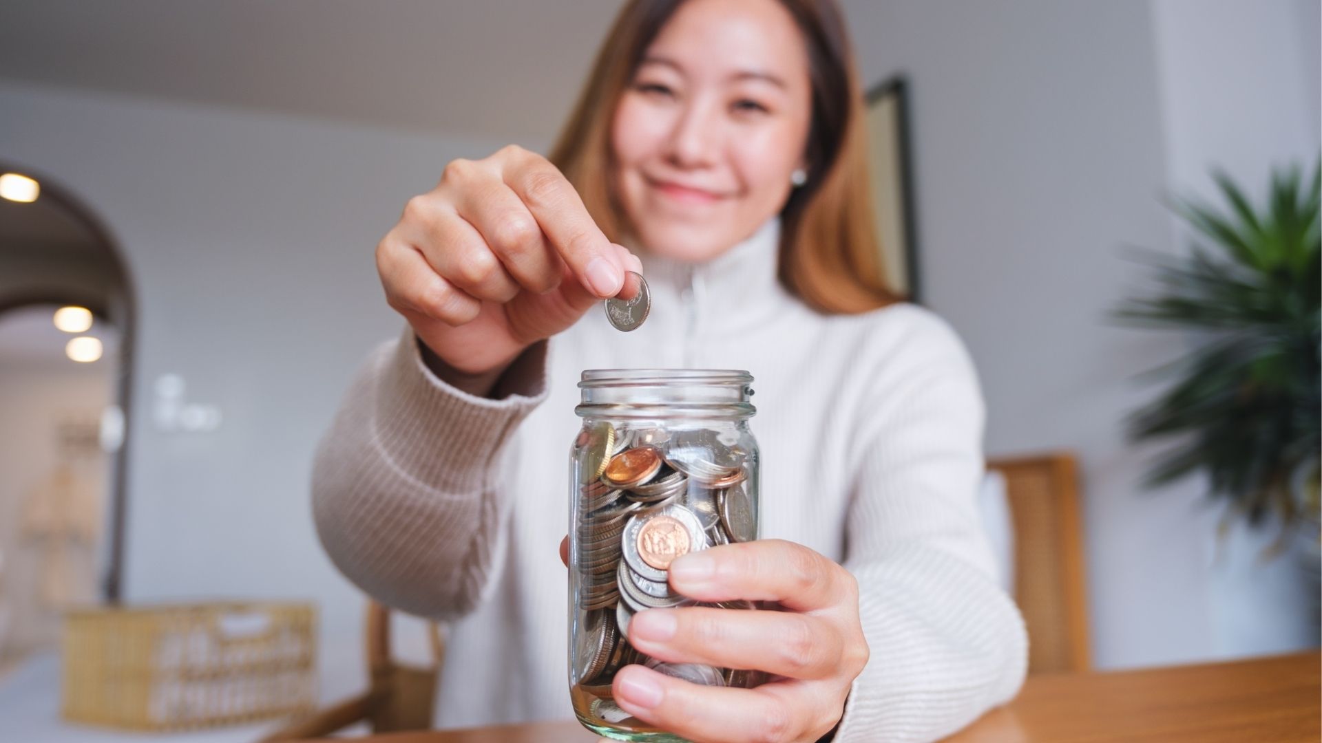 Woman collecting and putting coins in a glass jar for saving money 
