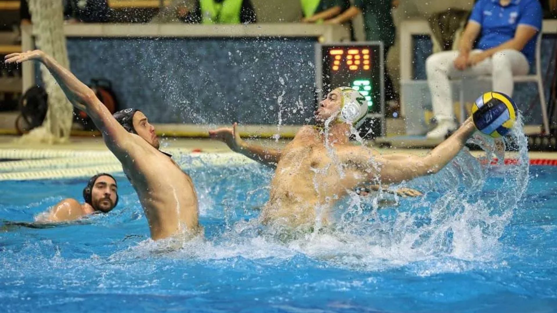 Water polo player attempts a powerful shot while a defender blocks in a crowded indoor pool.