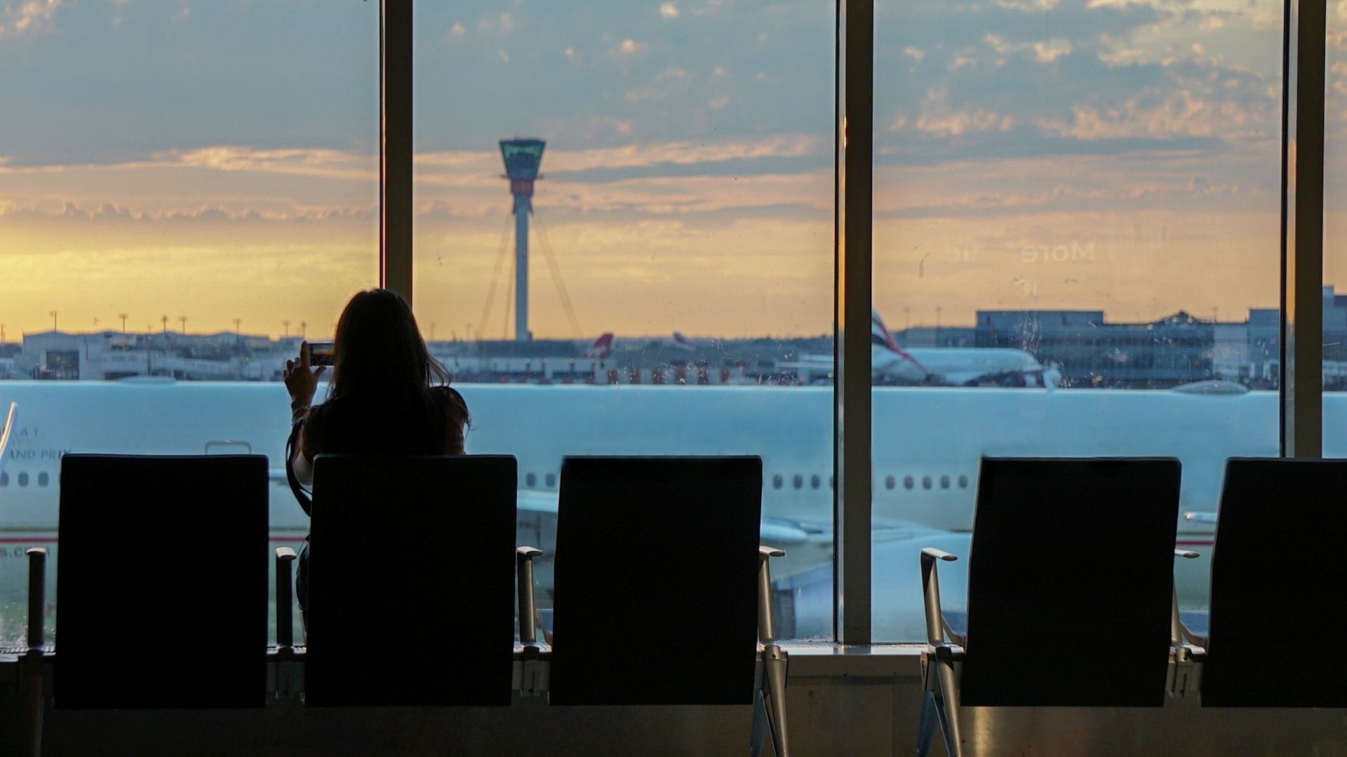 Woman taking photos of the view from an airport terminal, capturing the runway and cityscape beyond
