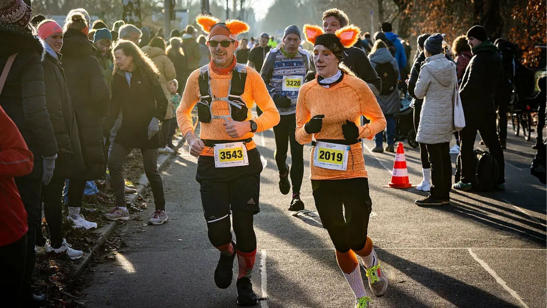 Runners in orange costumes with ear headbands jogging past spectators during a winter race