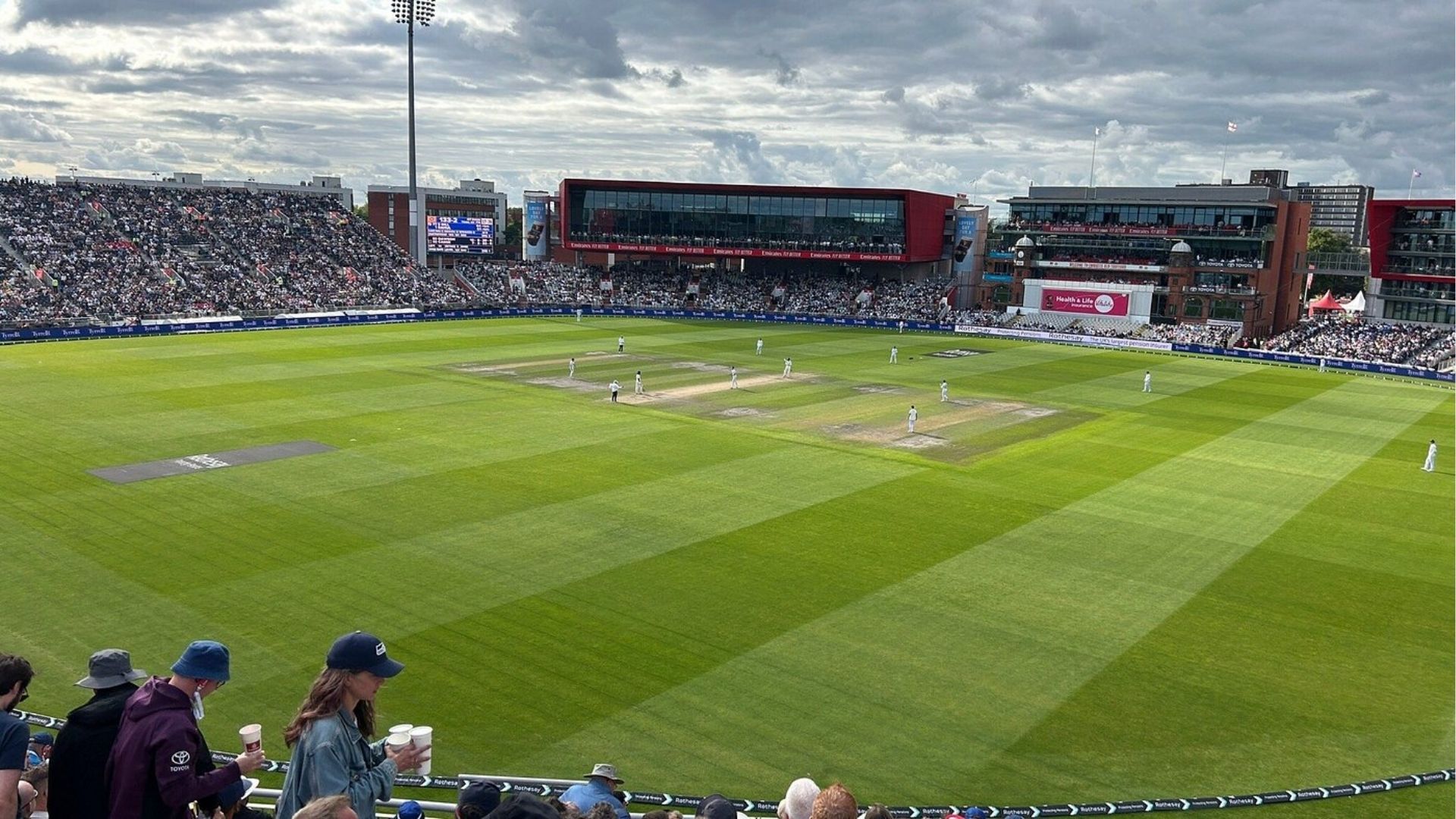 Daytime cricket match at a large stadium with full crowd and green outfield